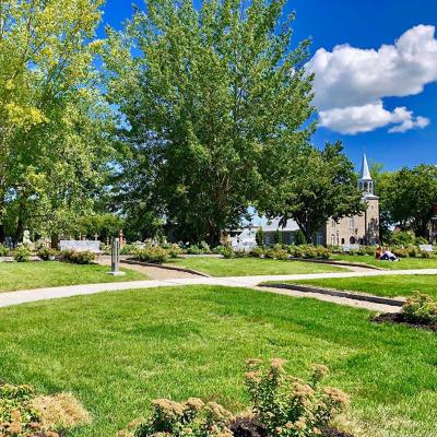 Les jardins du Centre d'art Diane-Dufresne, le cimetière et l'église en fond d'image.